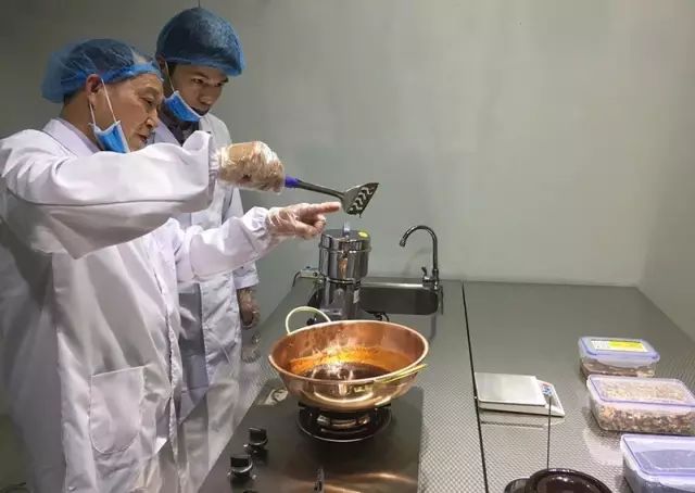 图为刘老师用金锅银铲熬制膏方样品并为学生讲解