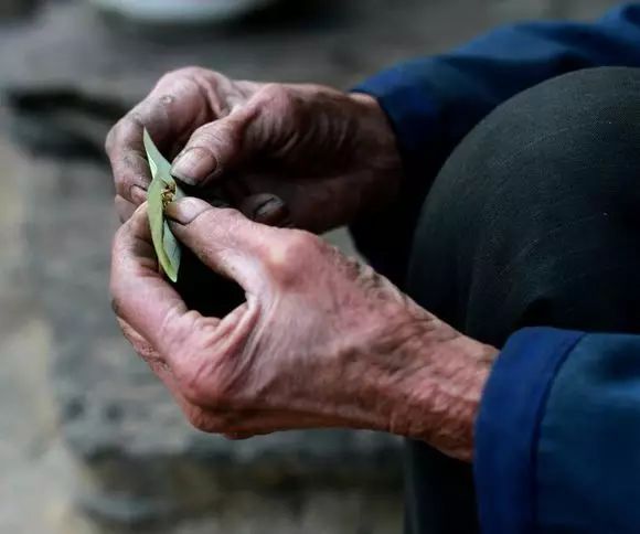 老人喜欢抽自己种的旱烟,他用费纸把烟丝放在纸上面卷成喇叭筒.