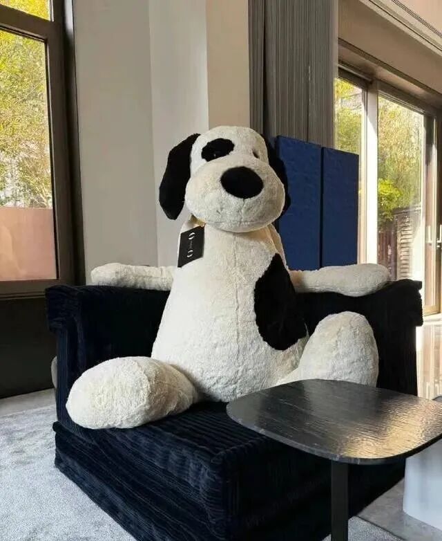 客厅落地窗旁的单人椅与大型玩偶摆件，强调柔软材质与休闲角落