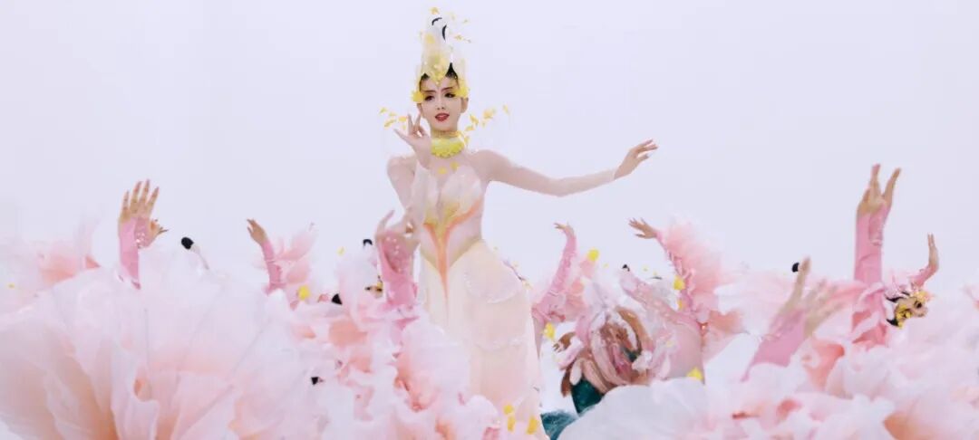 舞者身着粉白服饰带黄色点缀，与其他舞者在白色工作室表演