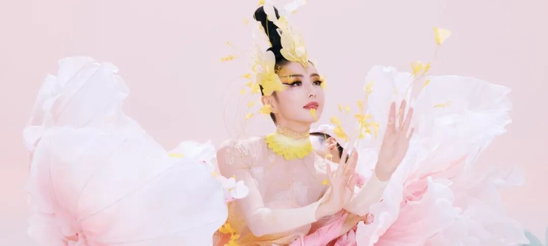 佟丽娅头戴黄色羽毛头饰，置身粉色花瓣中，背景梦幻