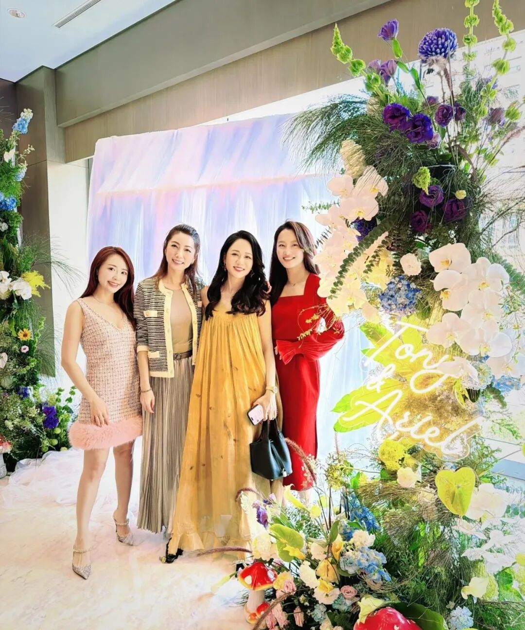 Four women stand together next to a floral arrangement and a sign reading To the Ariel.