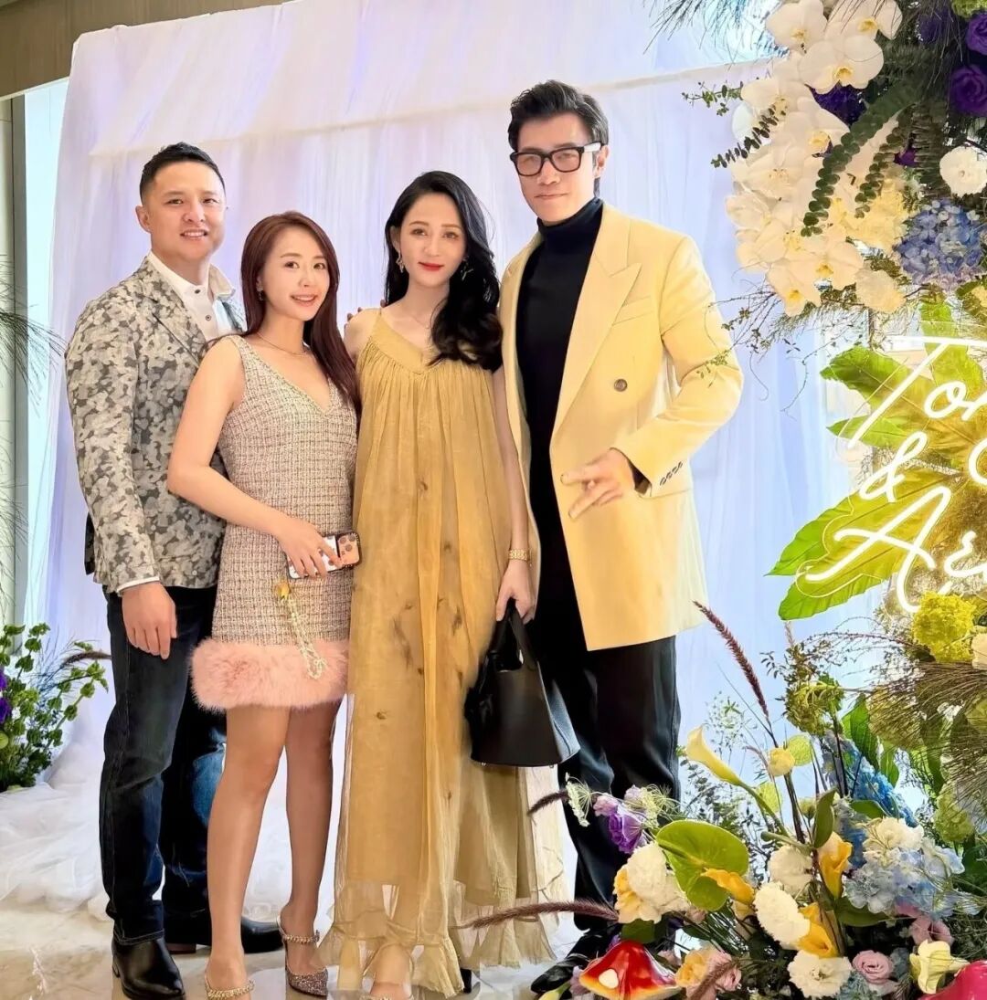 A group of four people dressed in fancy attire poses for a photo in front of a flower display