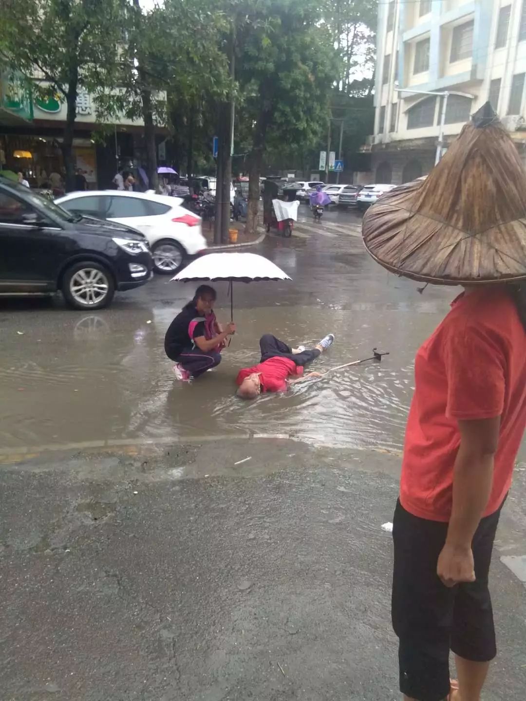 雨天路滑老人摔倒在拉堡街上,小姑娘孤独帮他打着伞,随后