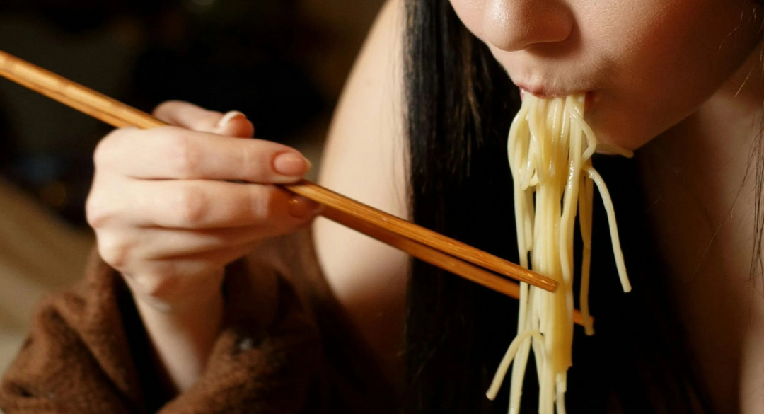 a woman eating a bowl of noodles with chopsticks