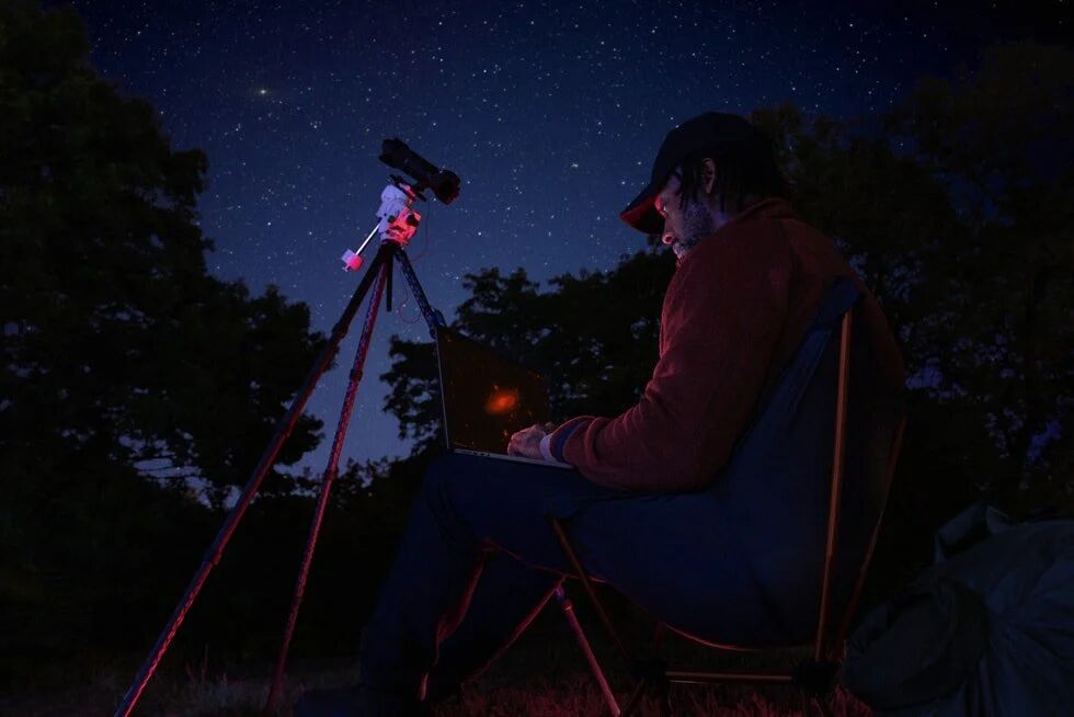 Image 8: A MacBook Pro user sits outside with a telescope under a starry night’s sky.