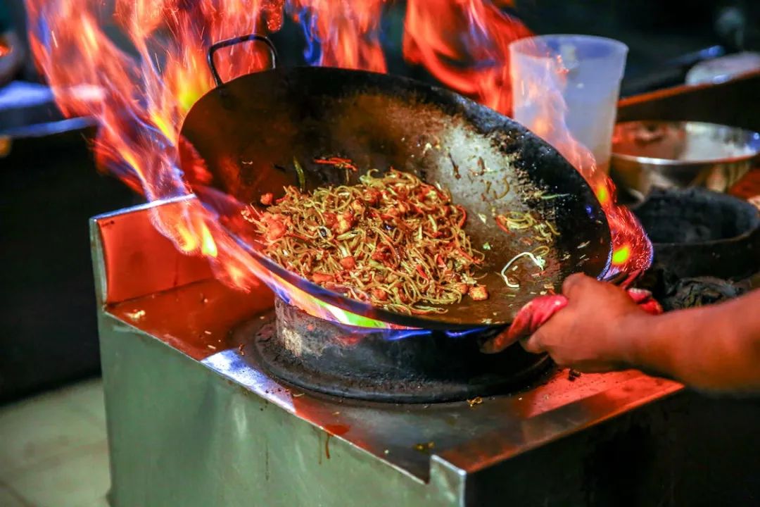 Free Vibrant close-up of chef cooking noodles in a flaming wok inside a restaurant kitchen. Stock Photo