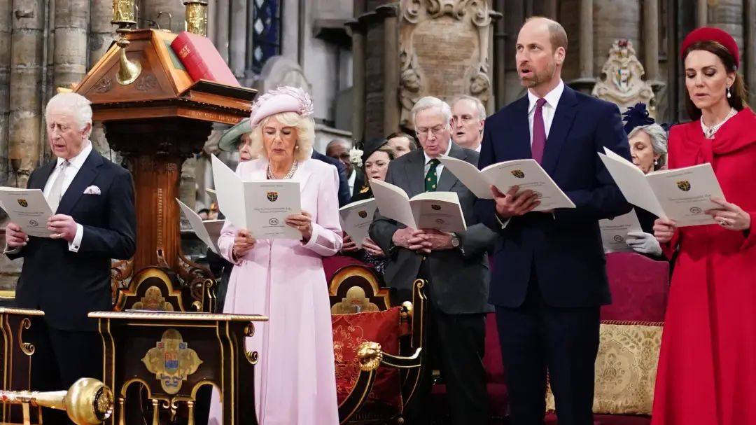 The King, Queen, Prince William and Catherine stand among a congregation of people inside a church as they sign from a hymn book.