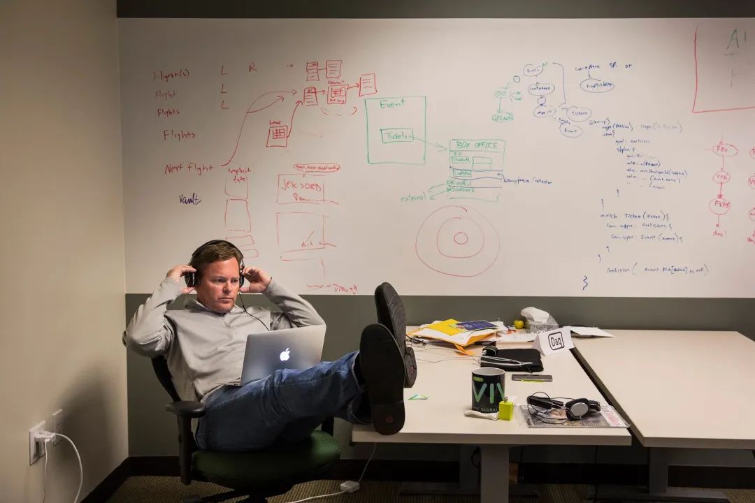 Dag Kittlaus sits with his laptop on his lap, feet up on a table, and headphones on