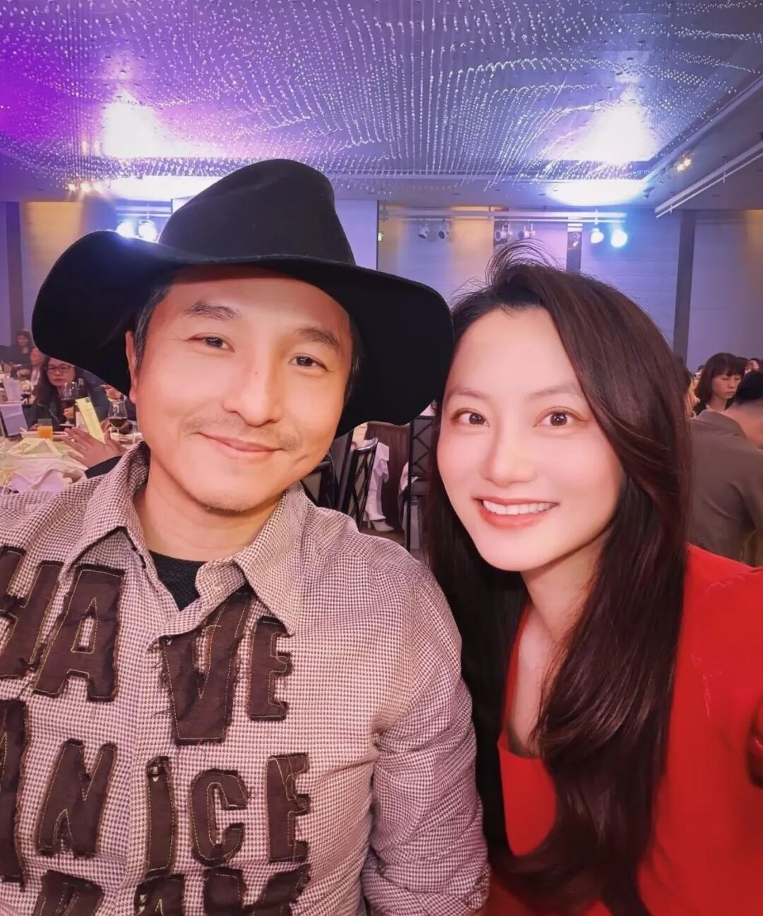 A couple is posing at a fancy event, the man in a cowboy hat and a shirt with the words have a nice day on it, the woman in a red dress