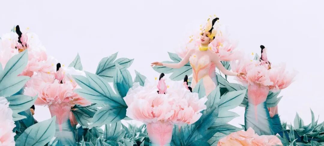 女性身着花卉主题服饰，置身巨型人造花中，场景奇幻