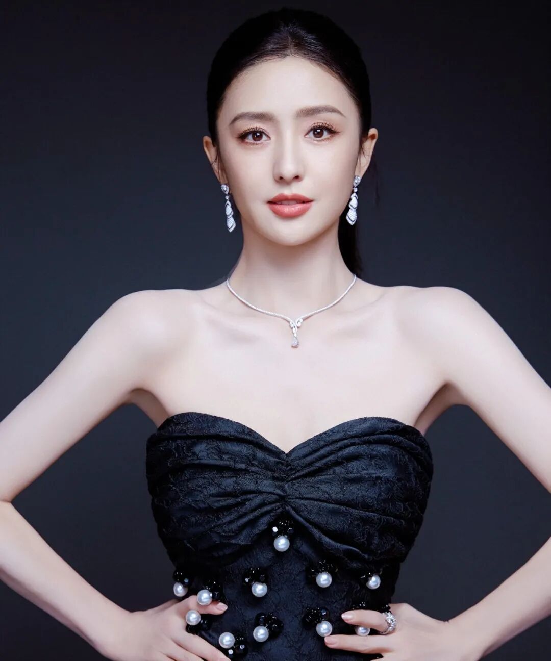 中国女性身着黑色无肩带礼服，妆容精致，背景深灰