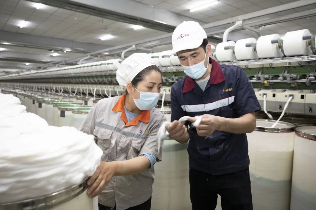 ▲艾山江·阿布都拉在纺纱车间检查纺纱质量，工作中的他格外认真。