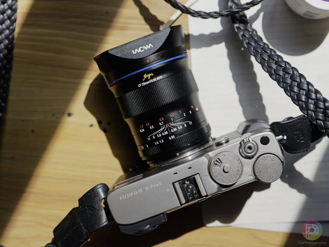 A Fujifilm X-Pro3 camera with a Laowa lens rests on a wooden surface in bright sunlight.