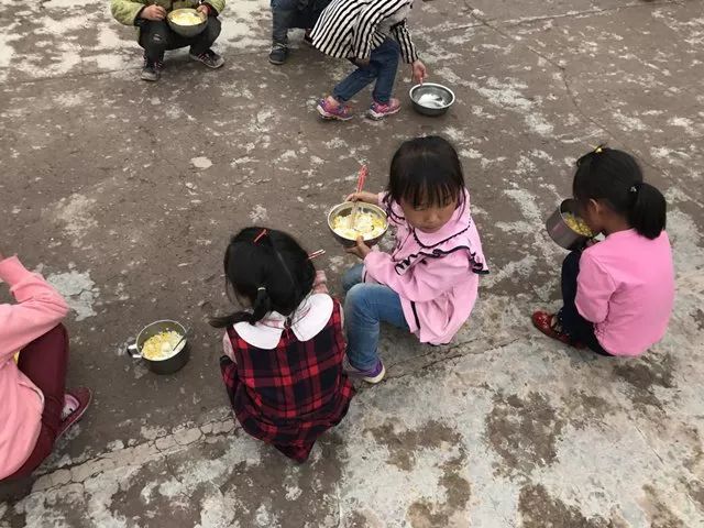 没有食堂,孩子们在操场空地上蹲着吃饭,可以看到,大部分人只有白饭和玉米粒