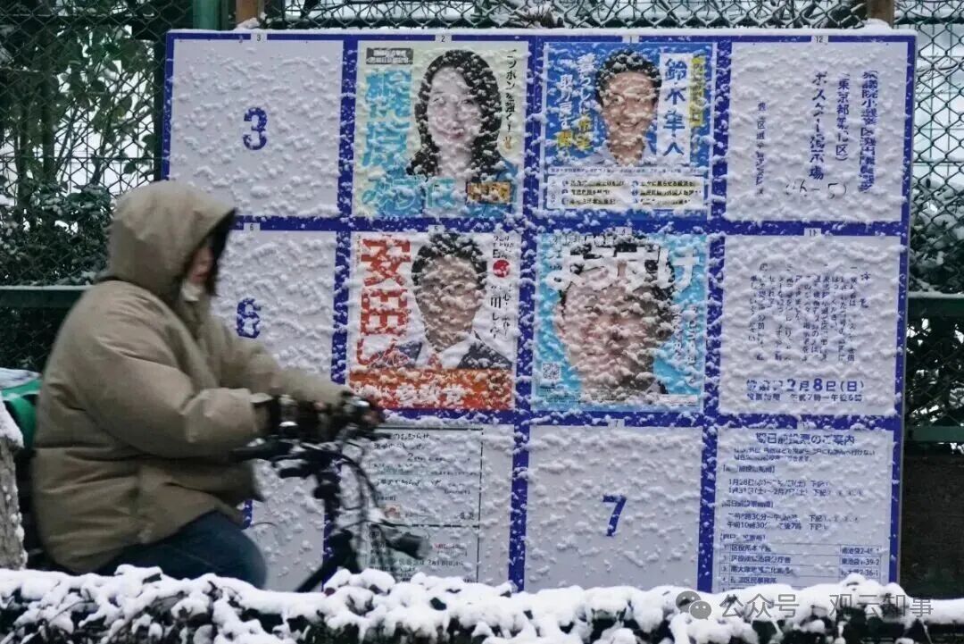 2月8日，东京雪花纷飞，行人骑车经过街头的选举广告牌。（来源：法新社）