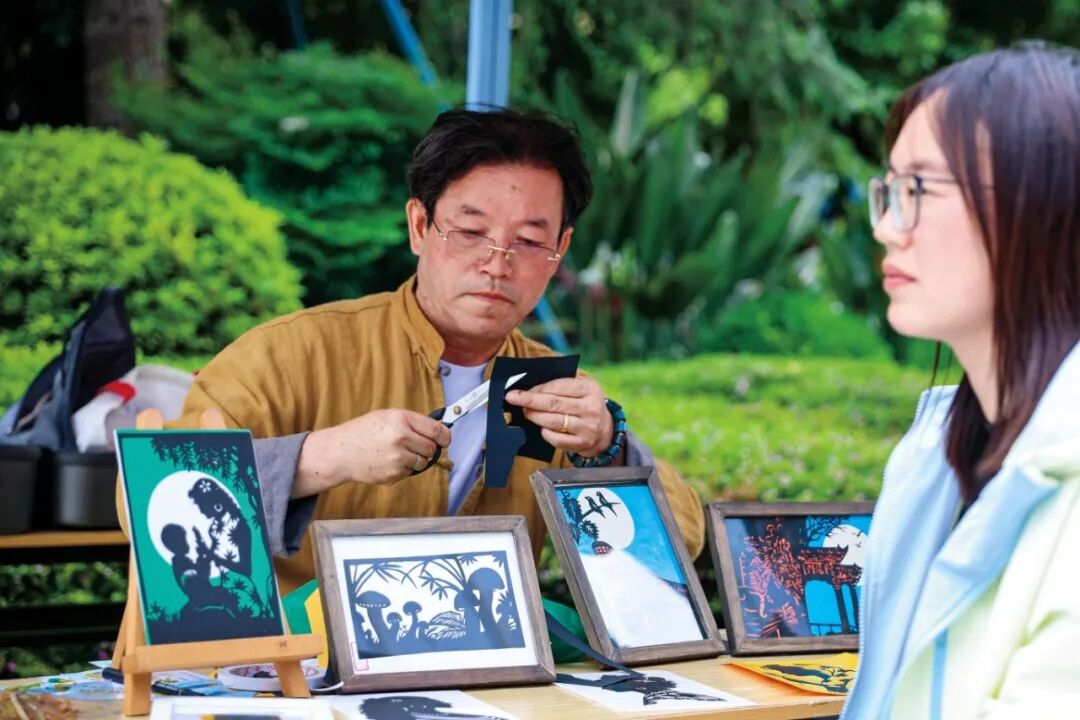 非遗体验区，非遗传承人正在根据青年职工的侧颜进行剪纸剪影。.jpg
