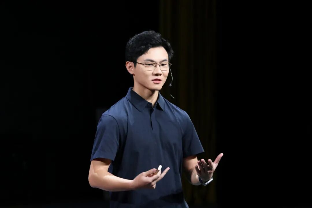 吴三岁在首届开智元学教育峰会台上演讲，黑色短袖，双手前伸
