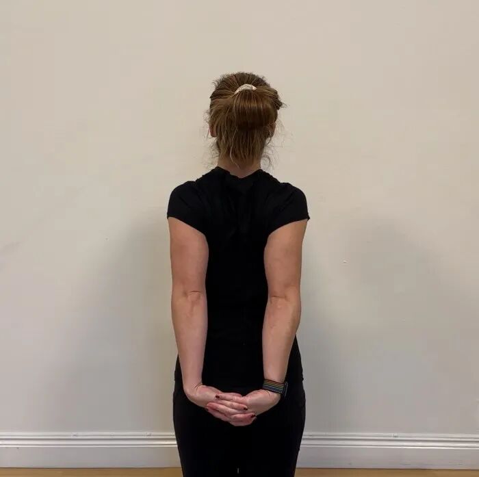 A photo of a woman doing a chest stretch with clasped hands behind her back.
