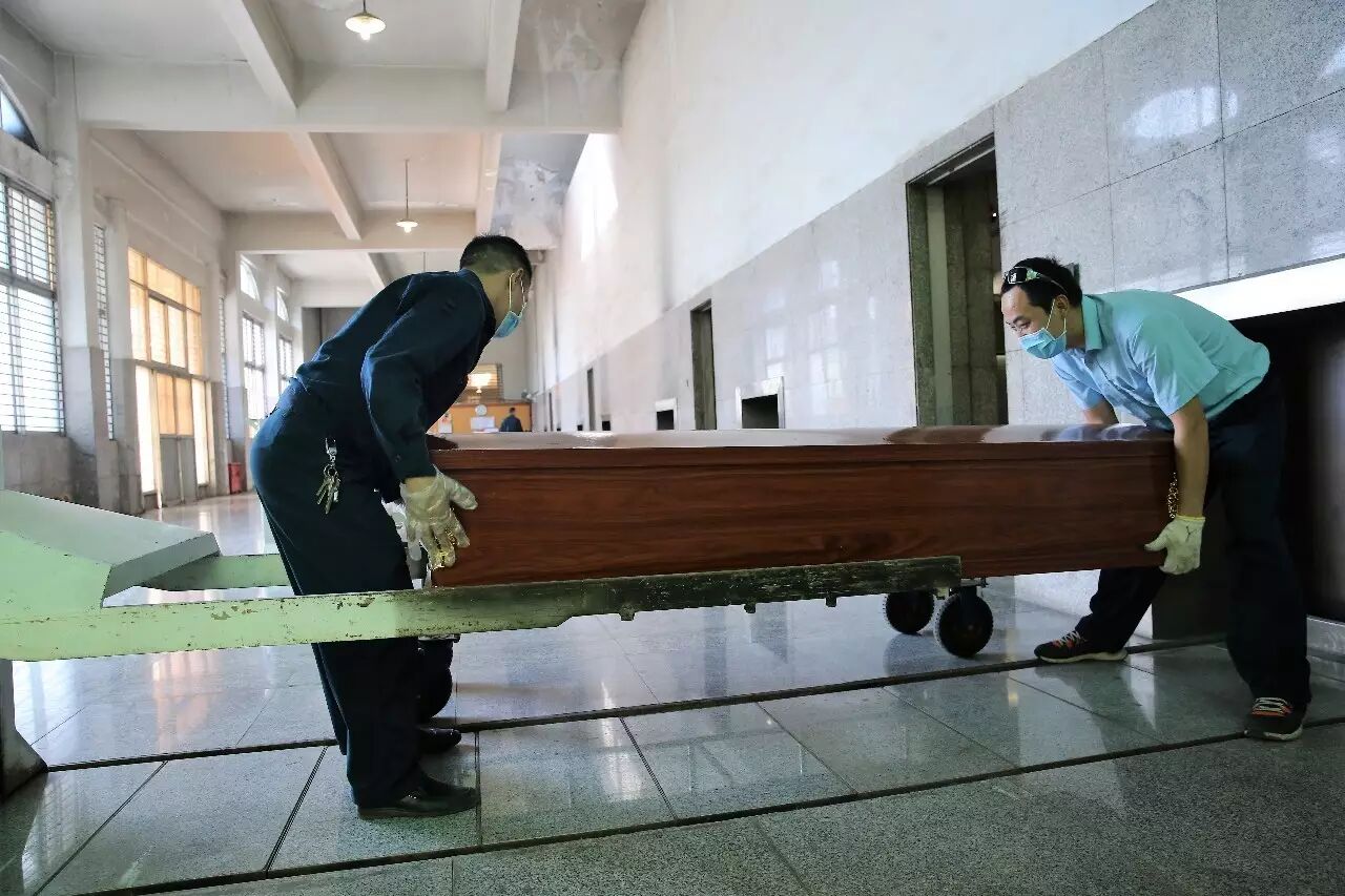 两名操作工将沉重的棺木搬上火化台.