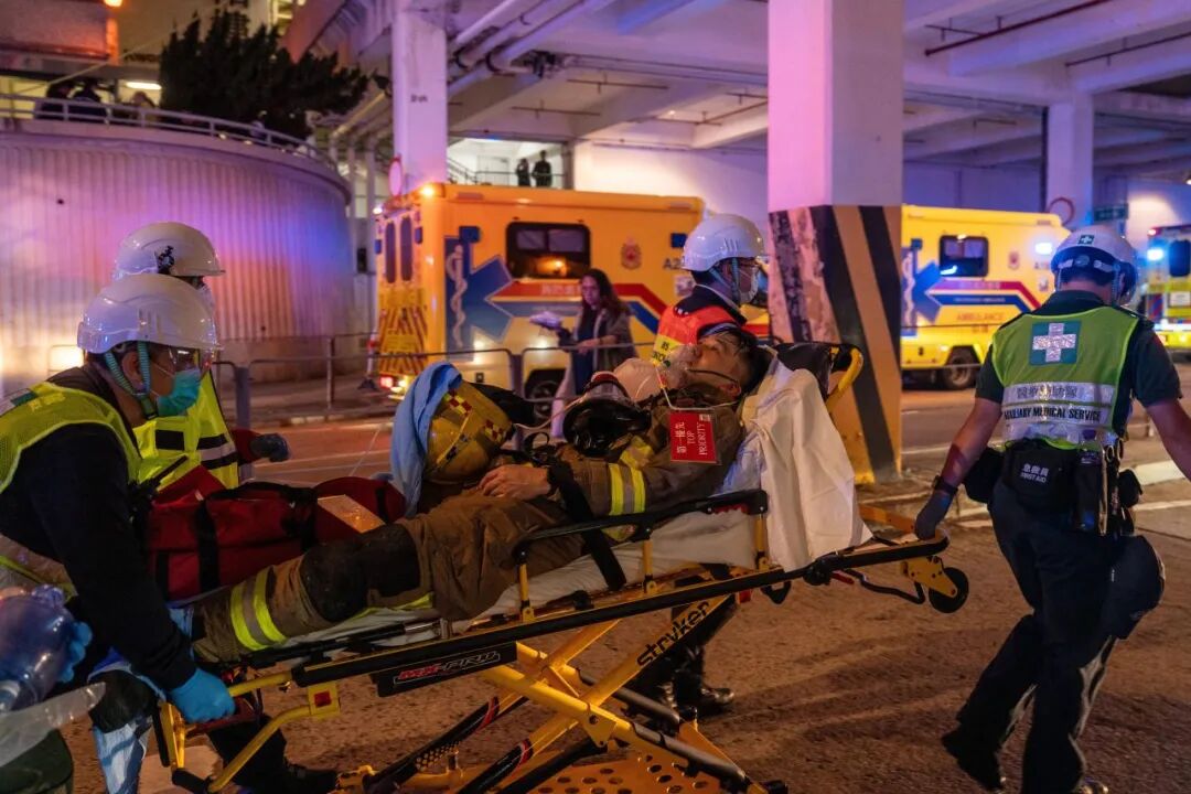 在火灾现场，医护人员用担架将一名消防员紧急送往救护车。（视觉中国 / 图）