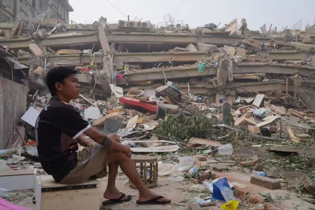 当地时间2025年3月30日,缅甸曼德勒Sky Villa住宅区,一位灾民静静地坐在倒塌房屋不远的地方。图/南方周末记者 翁洹