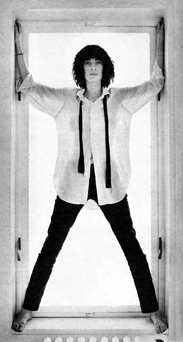 照片中patti smith发型凌乱,穿着男士白色衬衣,手提黑色西装外套,一条