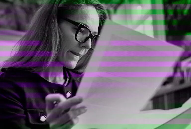A black and white photo of a woman with thick black spectacles reading text from sheets of paper