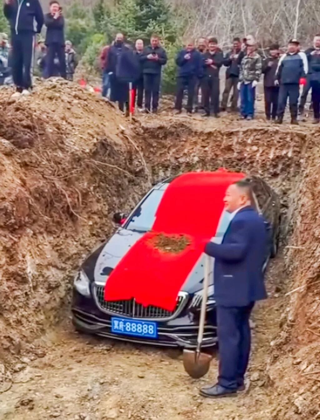 A mourner stands next to the about to be buried luxury car holding a spade. Photo: bilibili.com