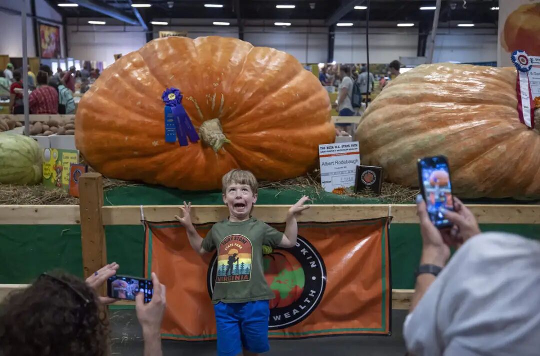 Theo Carrigan of Durham, poses for a photograph for his parents, with the prize-winning 2,123-pound giant pumpkin at the N.C. State Fair on Friday, October 16, 2026 in Raleigh, N.C.