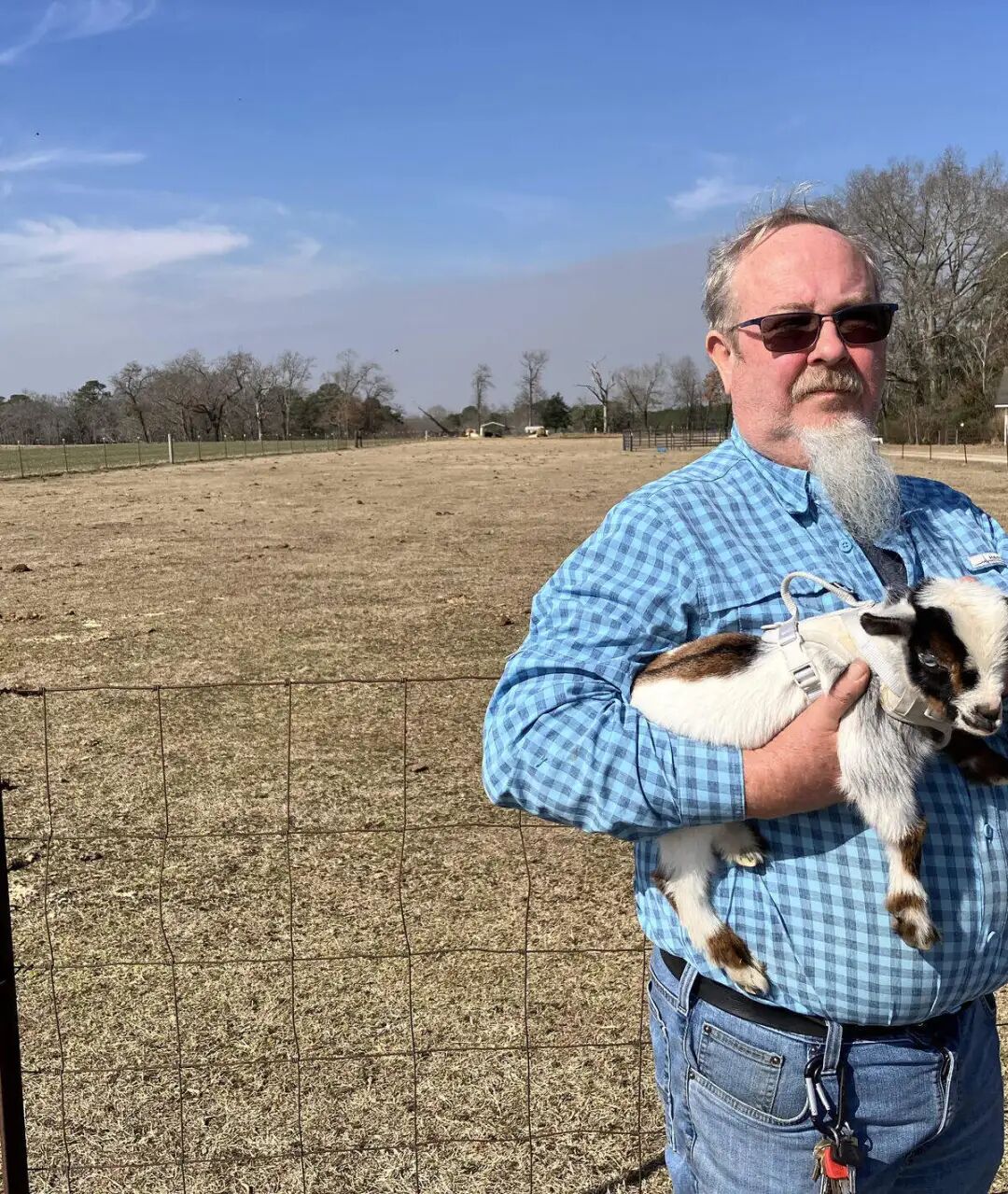 Farmer Robbie O’Neal holds his pet goat Feb. 10, 2026 while standing in front of an agricultural field that today is polluted with toxic forever chemicals. The family allowed industrial sludge from a textile plant to be used as a fertilizer after government regulators said it was safe.