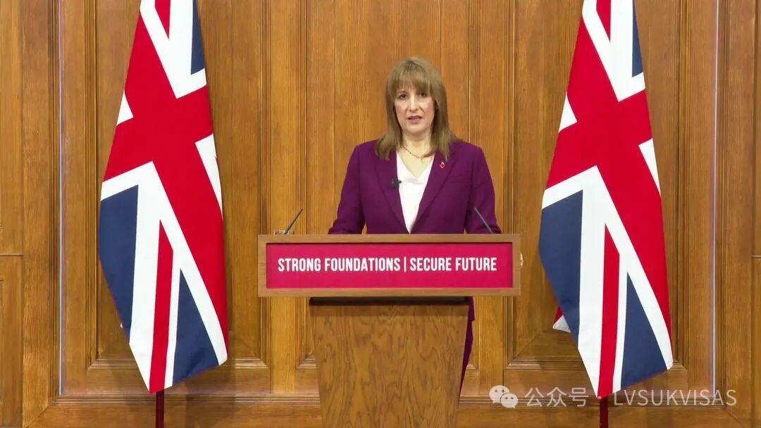 Chancellor Rachel Reeves giving a speech in the wood panelled Downing Street press conference suite between two union jack flags at a lecturn with the words Strong Foundations Secure Future. She is wearing a purple blazer and pale pink v neck top