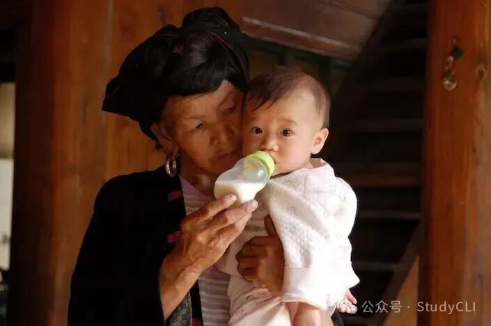 a Chinese ethnic minority woman in traditional dress feeds a bottle to a baby that she's holding in her arms
