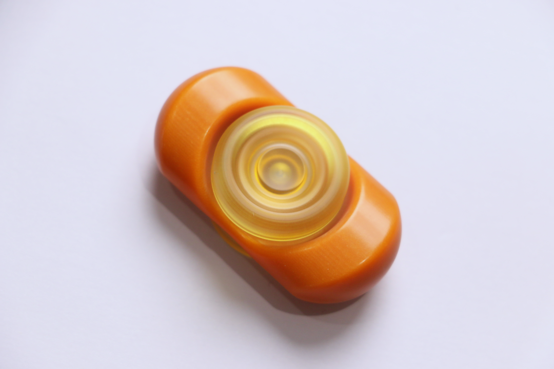An orange Bakelite Yuandian spinner rests diagonally on a pale surface, with a pale yellow central button