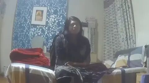 Undercover footage of an Asian woman sitting on a bed. The chimney breast behind her has been turned into a feature wall with bright blue and silver wallpaper, while the bed cover is a large check pattern in yellow, blue and  grey.