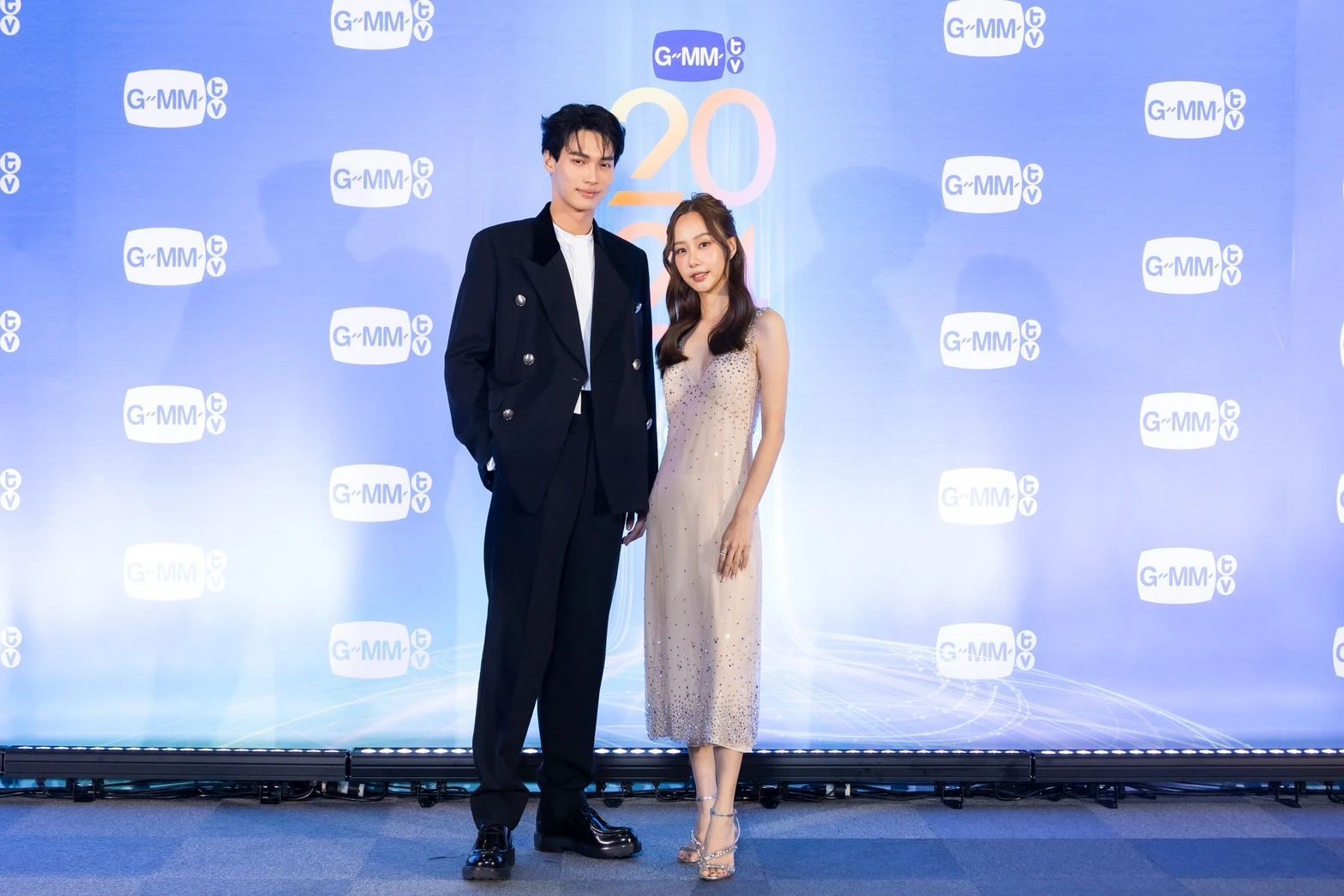 A person and person standing in front of a blue backdropDescription automatically generated