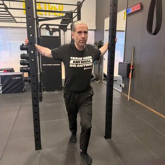 A photo of a man doing a doorway stretch for the pecs, but between two crosscage frame columns.