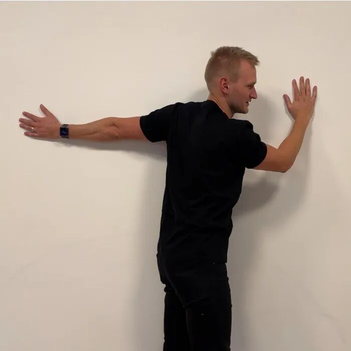 A photo of a man doing a wall chest stretch.