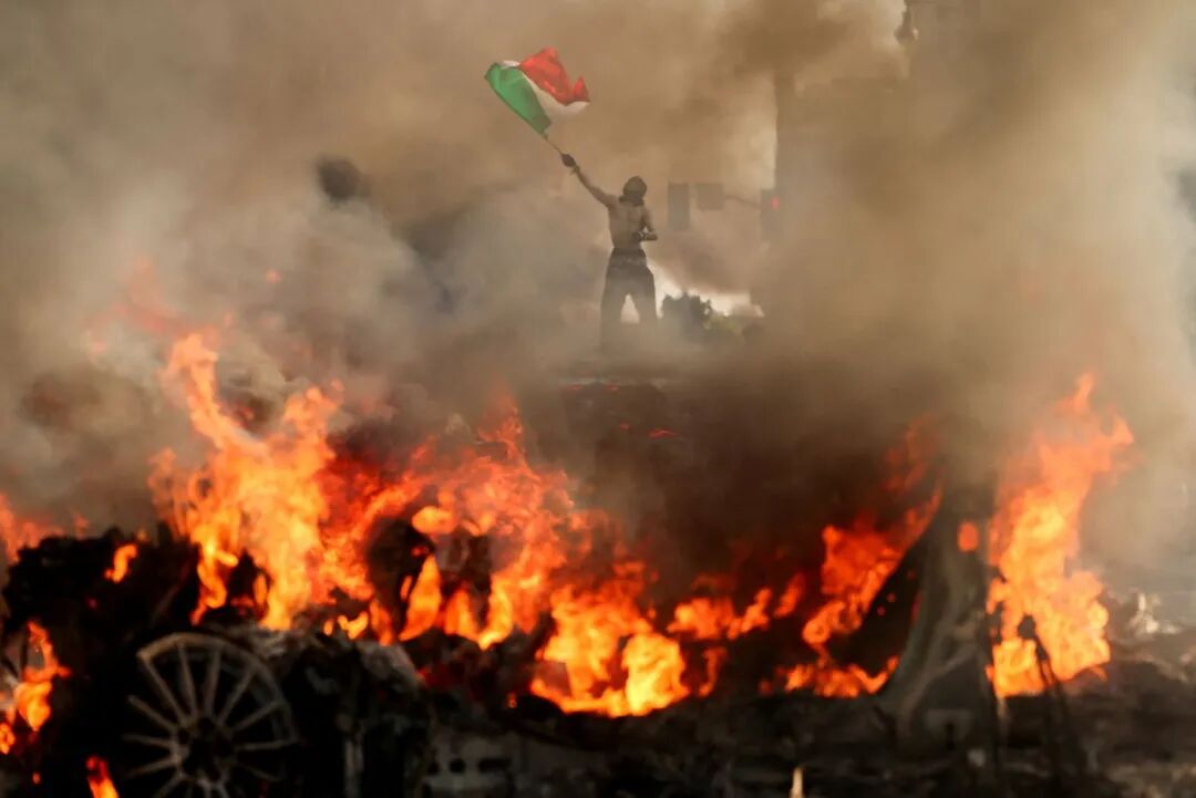 A man waves a Mexican flag as smoke and flames rise from a burning vehicle during a protest against federal immigration sweeps, near Los Angeles City Hall in downtown Los Angeles, California, on Sunday.