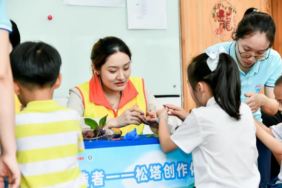在松塔创作体验摊位，志愿者教孩子们用松果制作不同的小动物