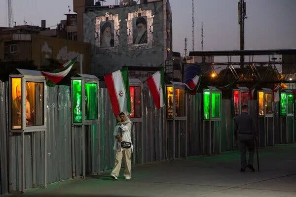 一名女子走过一面装饰着伊朗国旗和灯火通明的肖像的墙。