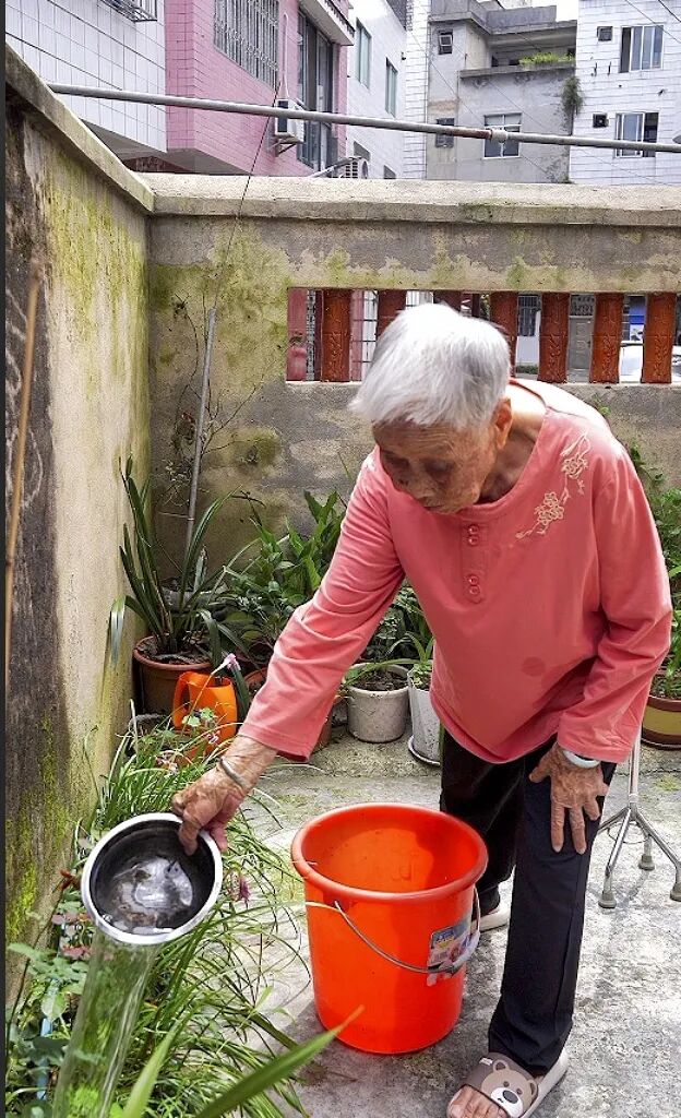 莫月仙在给院子里的绿植浇水。104岁的她，仍保持着对生活的热爱。