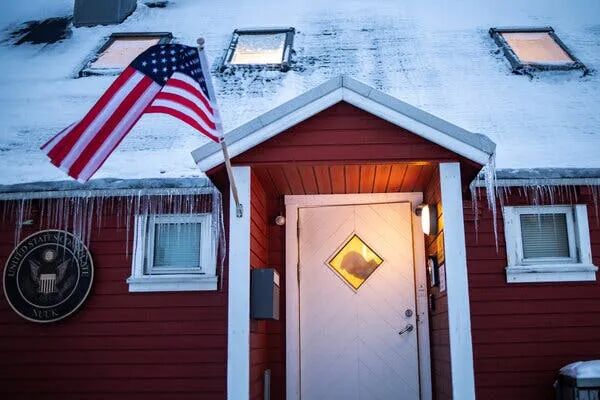 A low, red-painted building with a white door, a U.S. flag and a plaque saying “United States Consulate.”
