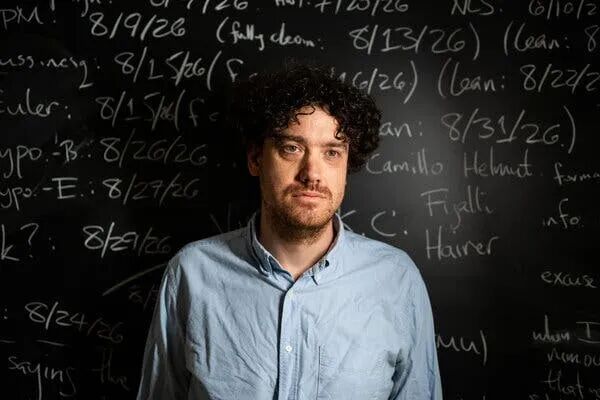Tristan Buckmaster standing in front of a chalk blackboard with various dates and names written on it.