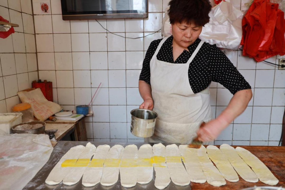 辛广云在擀好的朝牌面饼上刷油（刘新梅 摄）2.png